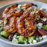 Fresh grilled shrimp sit atop a vibrant Greek Shrimp Bowl with diced cucumber, cherry tomatoes, red onion, and crumbled feta cheese, drizzled with a zesty lemon-olive oil dressing.