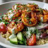 Colorful Mediterranean shrimp bowl featuring pink shrimp, olives, tomatoes, and a drizzle of tangy tahini dressing.