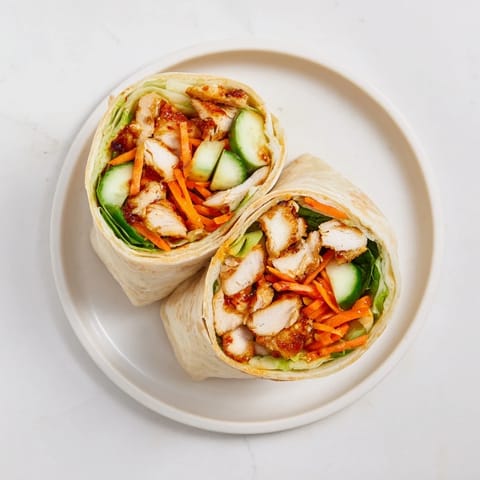 A warm Honey Chili Crunch Chicken Wrap sliced to reveal layers of honey-glazed chicken, crunchy lettuce, and shredded carrots.