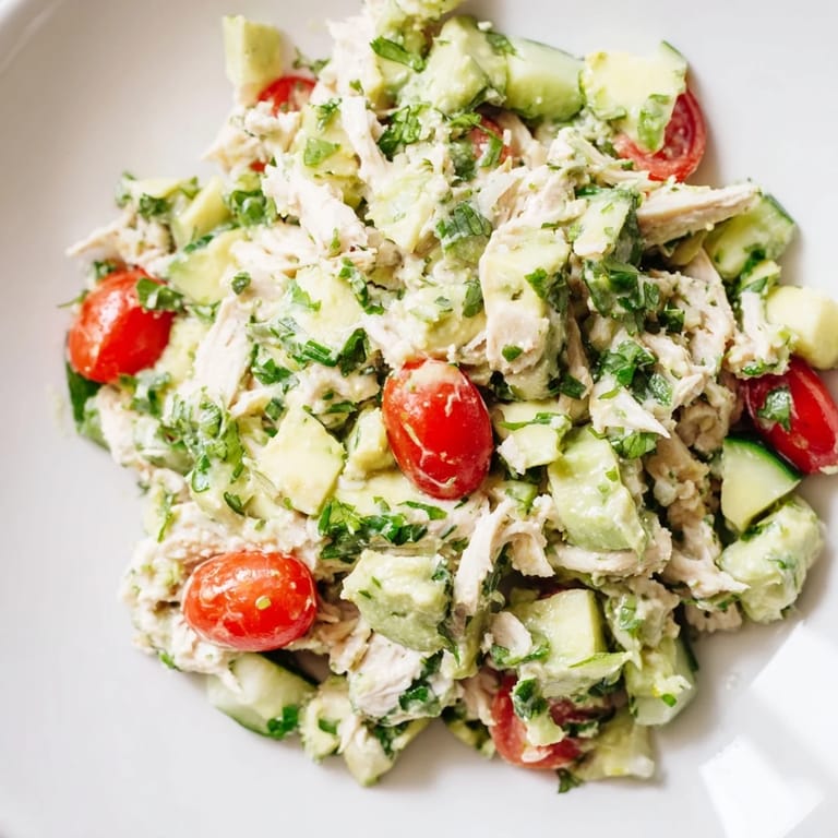 Healthy avocado chicken salad garnished with cilantro and lime wedges, tossed in olive oil for a zesty American-style meal.